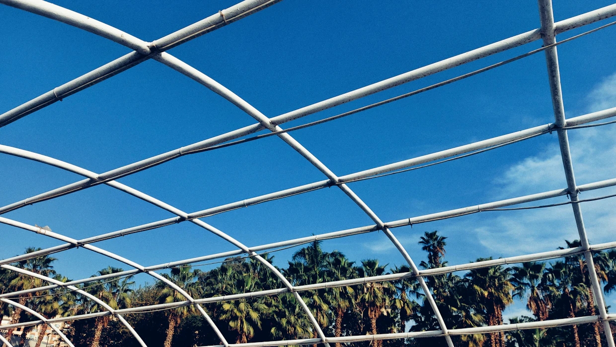 Screen enclosure framing and mesh roof panels seen from inside against bright sky